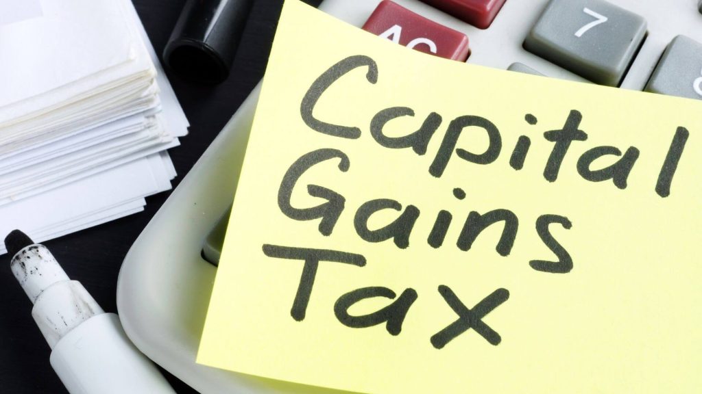 Close-up of a handwritten note labeled 'Capital Gains Tax' next to a calculator and financial documents, suggesting preparation by a property investor for tax calculations.