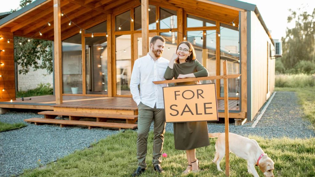 Selling a house in South Australia - a couple standing beside a 'For Sale' sign outside a modern, wooden house, showcasing their pet dog, illustrates the process of selling a house in South Australia, highlighting the lifestyle and appeal of property in a scenic outdoor setting.