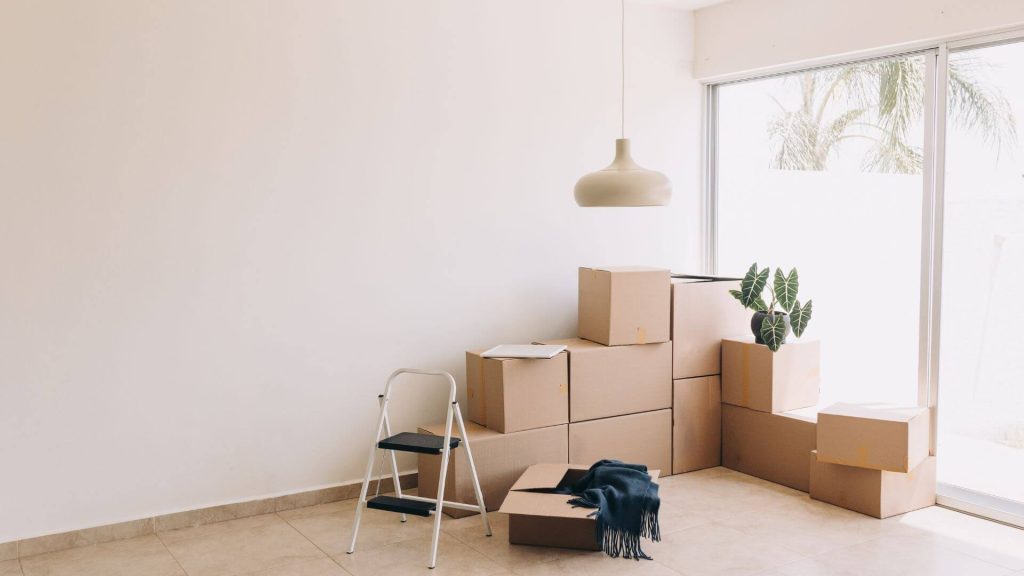 Packed moving boxes stacked near a large window, signifying the process of ending a tenancy and preparing to vacate a rental property. Ending a tenancy can involve careful planning, especially regarding notice periods and finalising lease agreements.