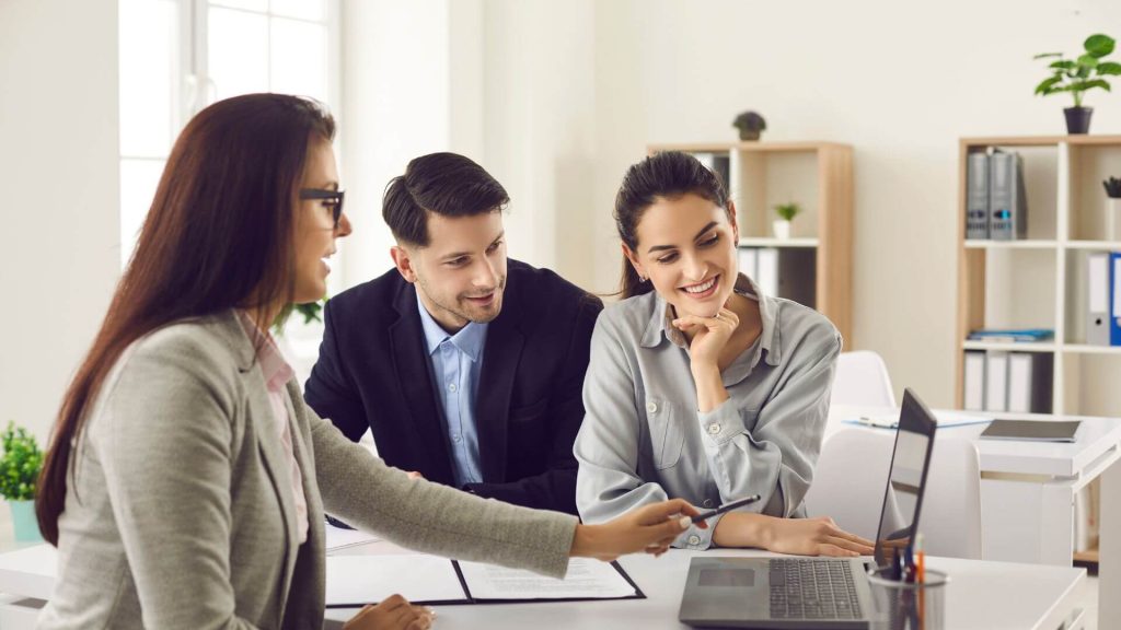 Three professionals discussing strategies for property investors around a laptop, focusing on financial planning and loan repayment options.